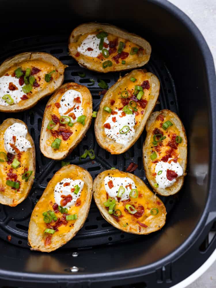 Top view of air fryer potato skins in an air fryer garnished with sour cream, green onions, and bacon.