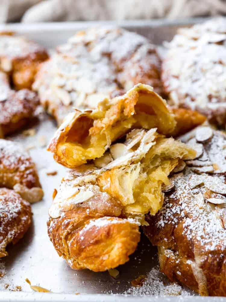 Closeup of an almond croissant broken in half, dusted with powdered sugar.