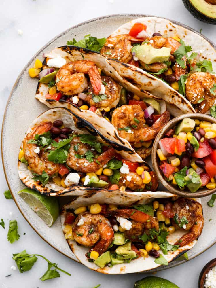 A platter with 4 blackened Cajun shrimp tacos with a small bowl of avocado salsa. 