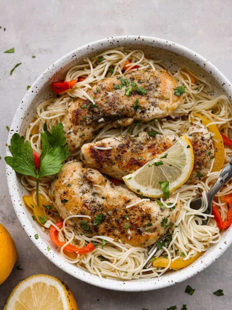 Chicken scampi served with angel hair pasta in a white stoneware bowl, garnished with fresh parsley and a lemon slice.