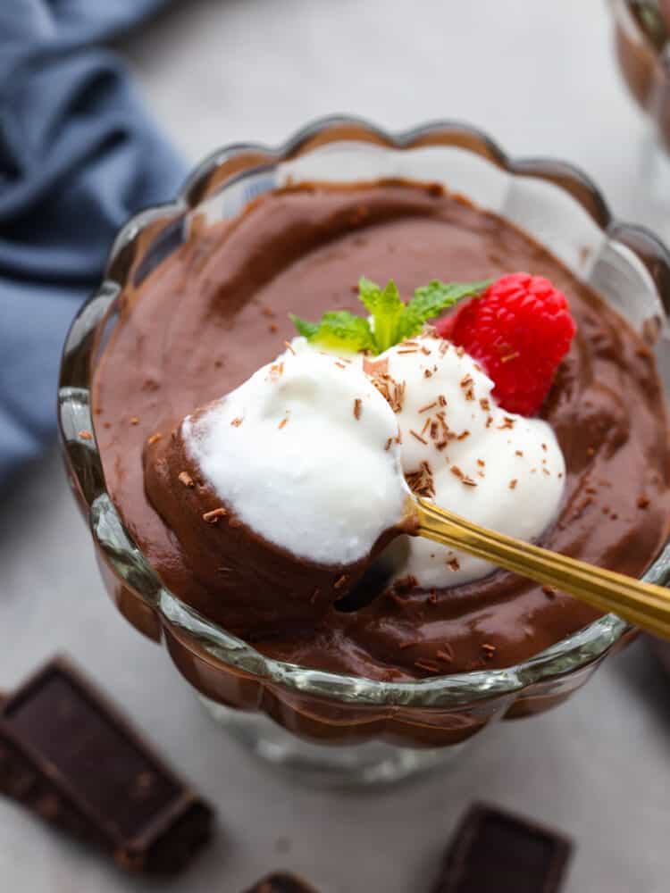 Closeup of chocolate pudding in a glass jar, garnished with whipped cream and a raspberry.