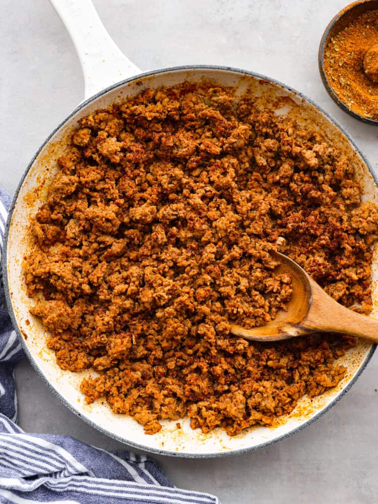 Chorizo ground pork in a white pan with a wooden spoon taking a scoop out.