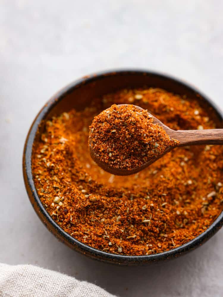 Closeup of chorizo seasoning blend in a black bowl, being scooped up with a small wooden spoon.