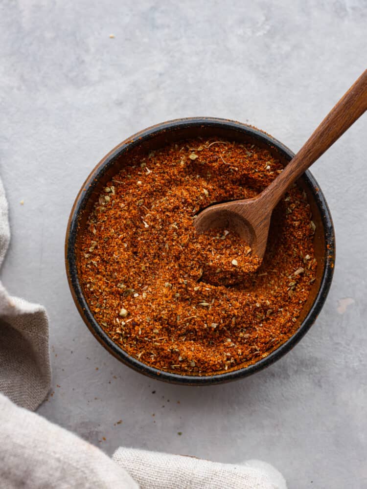 Top-down view of chorizo seasoning blend in a black bowl. There is a wooden spoon in it.