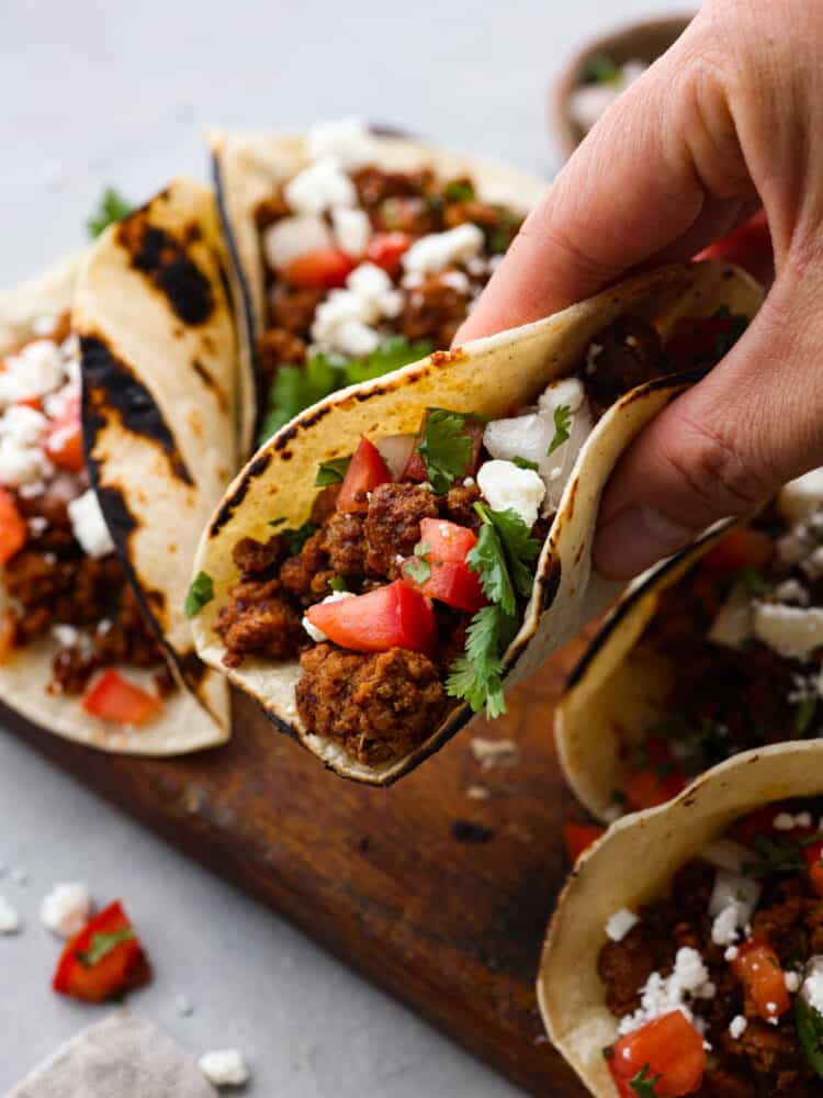 A hand holding a Mexican Chorizo Taco with other tacos in the background.