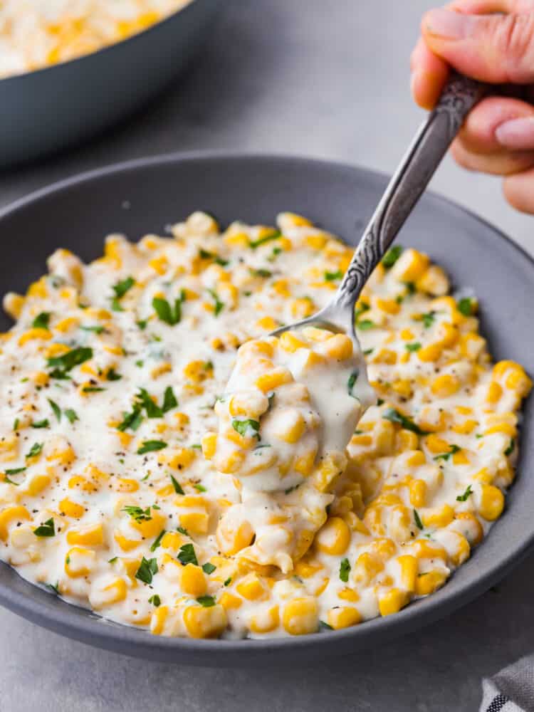 Closeup of corn cream in a gray bowl picked up with a metal spoon.