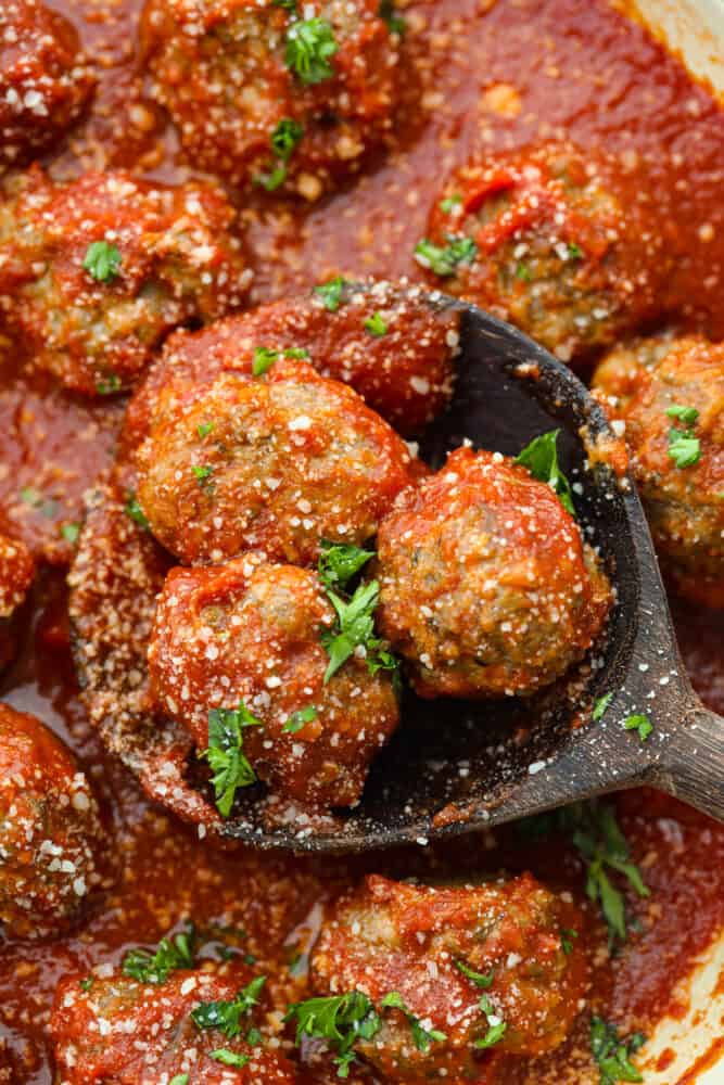 Closeup of 3 meatballs in a wooden spoon.