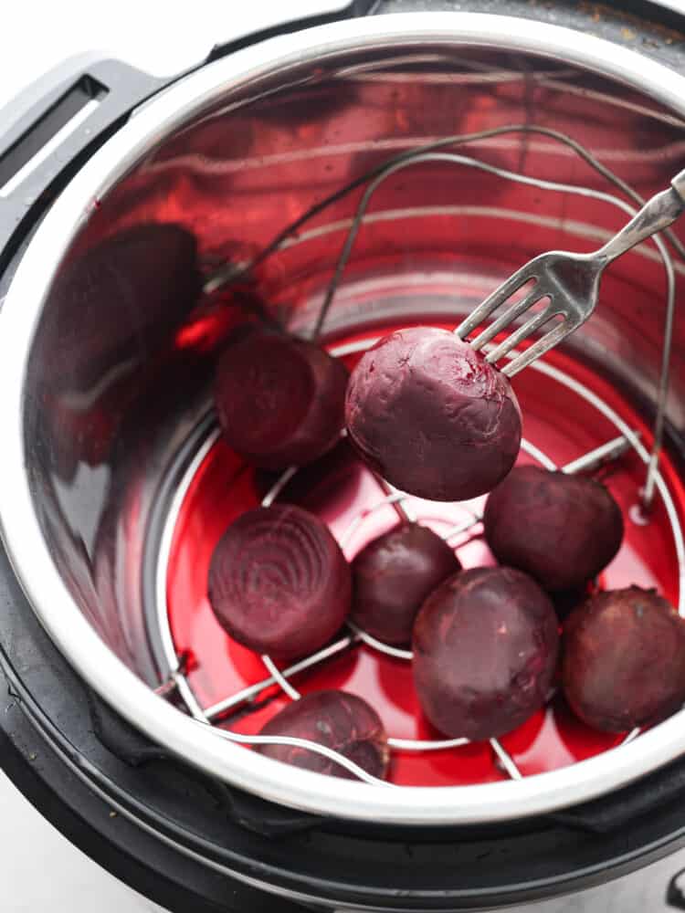 Multiple cooked beets in the trivet of an Instant Pot can be seen. One is skewered with a fork.