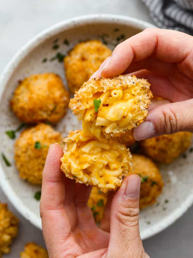 Someone holding a Mac and cheese ball that is broken in half. 