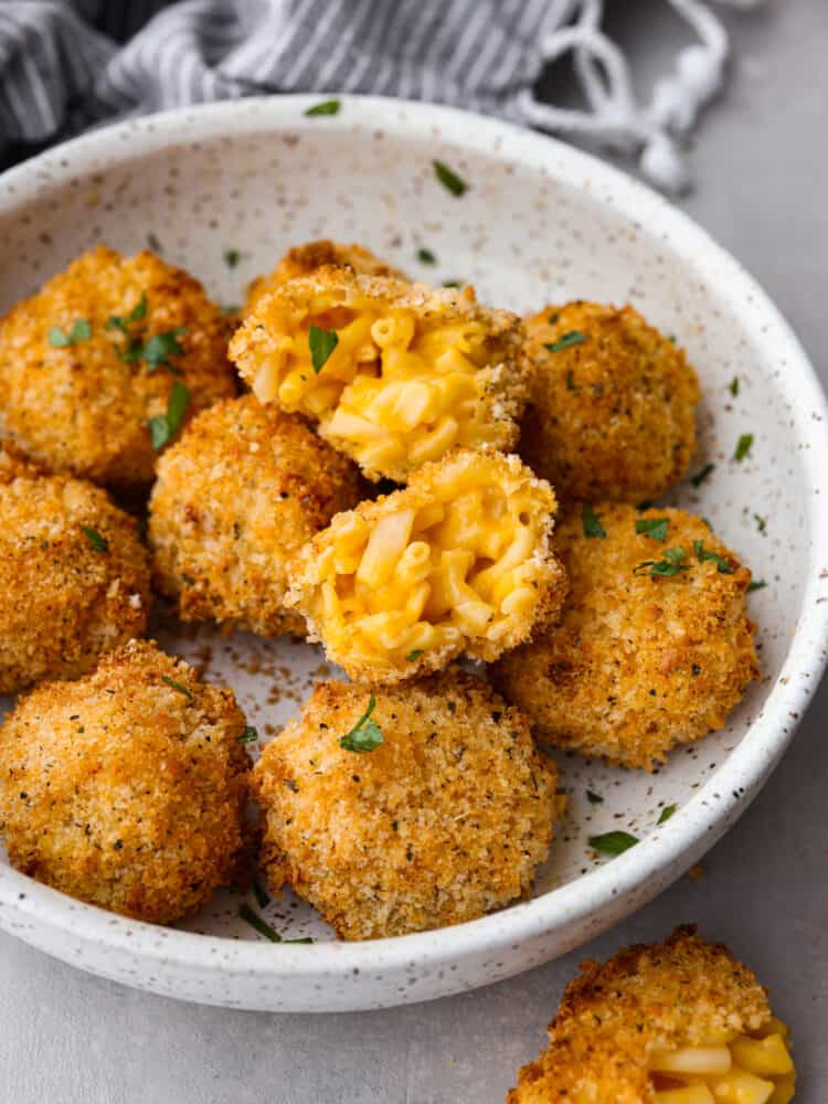A bowl of Mac and cheese balls, one on top that is broken open. 