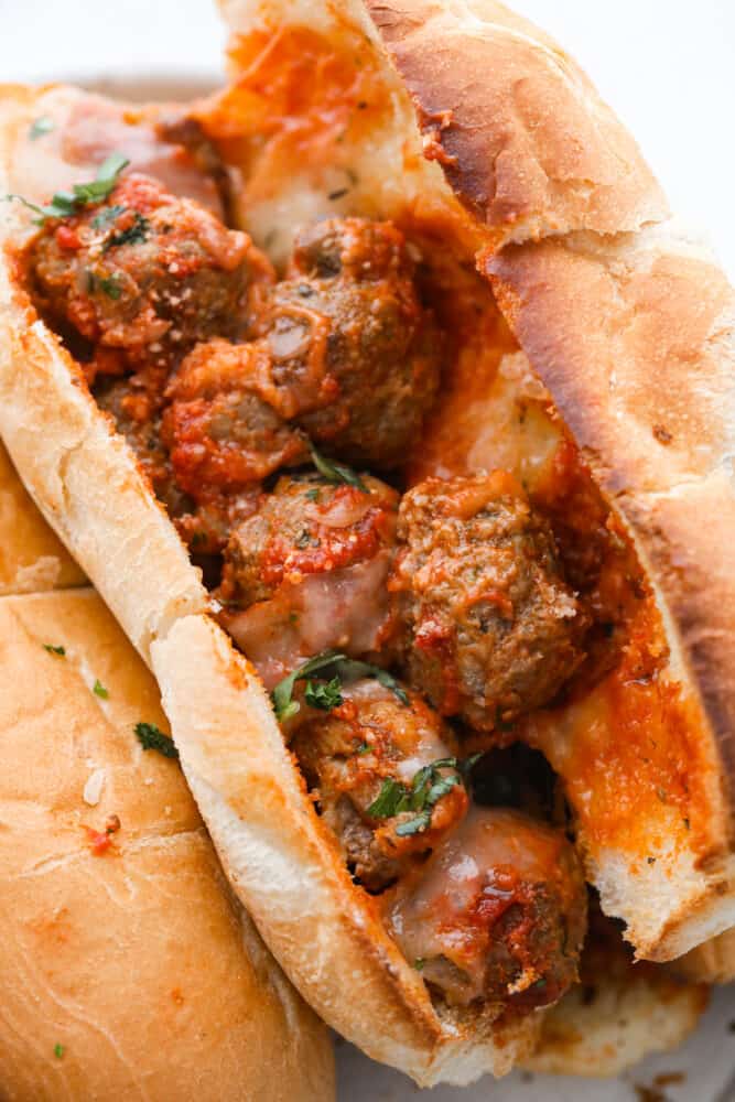 Close up view of a meatball sub open and filled with meatballs and marinara.  Garnish with chopped basil on top.