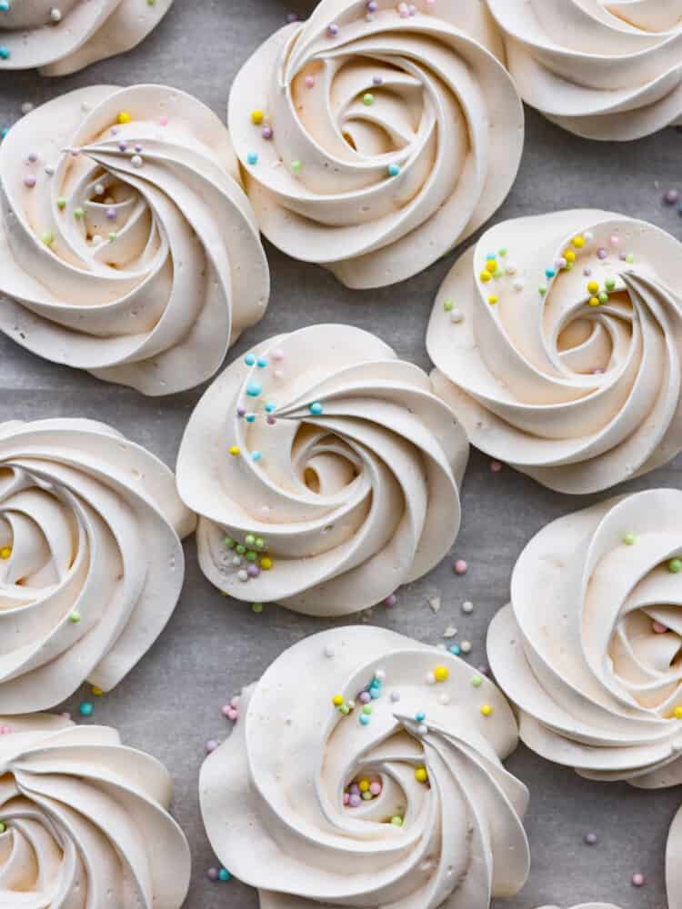 Meringue cookies with colorful sprinkles on top sitting on top of parchment.