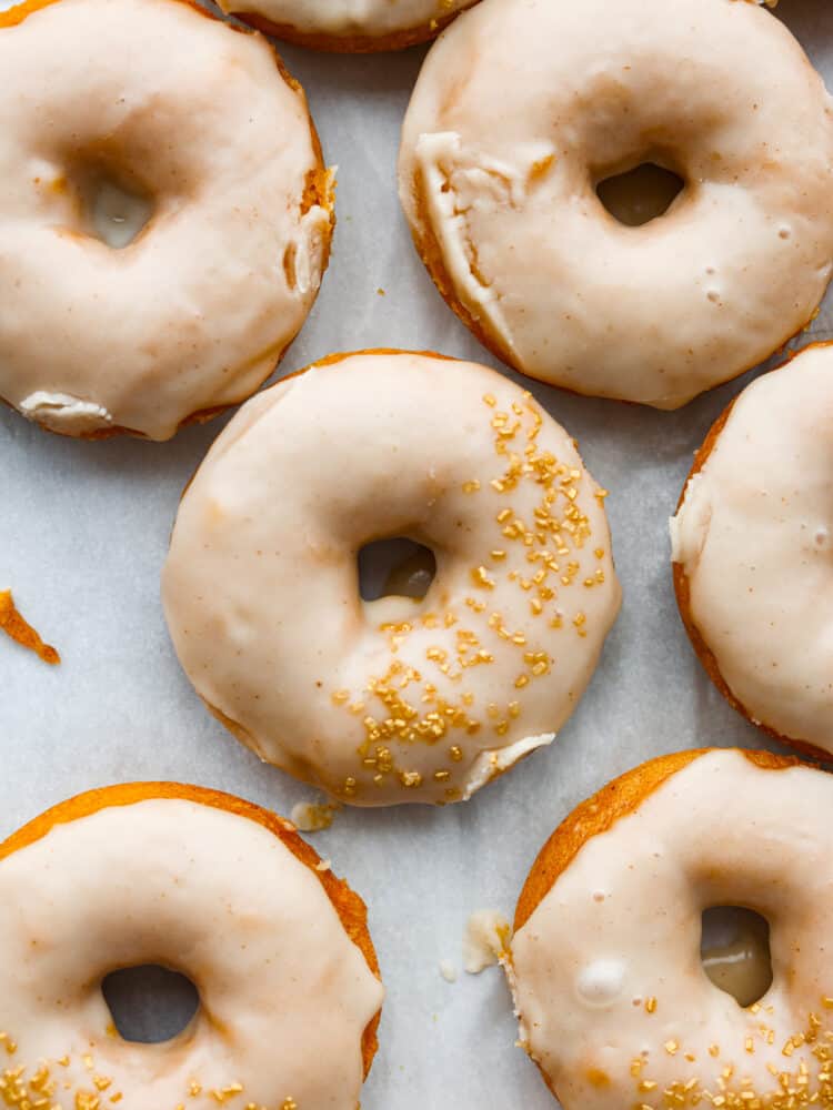 Pumpkin donuts with brown butter frosting laid out on parchment paper.