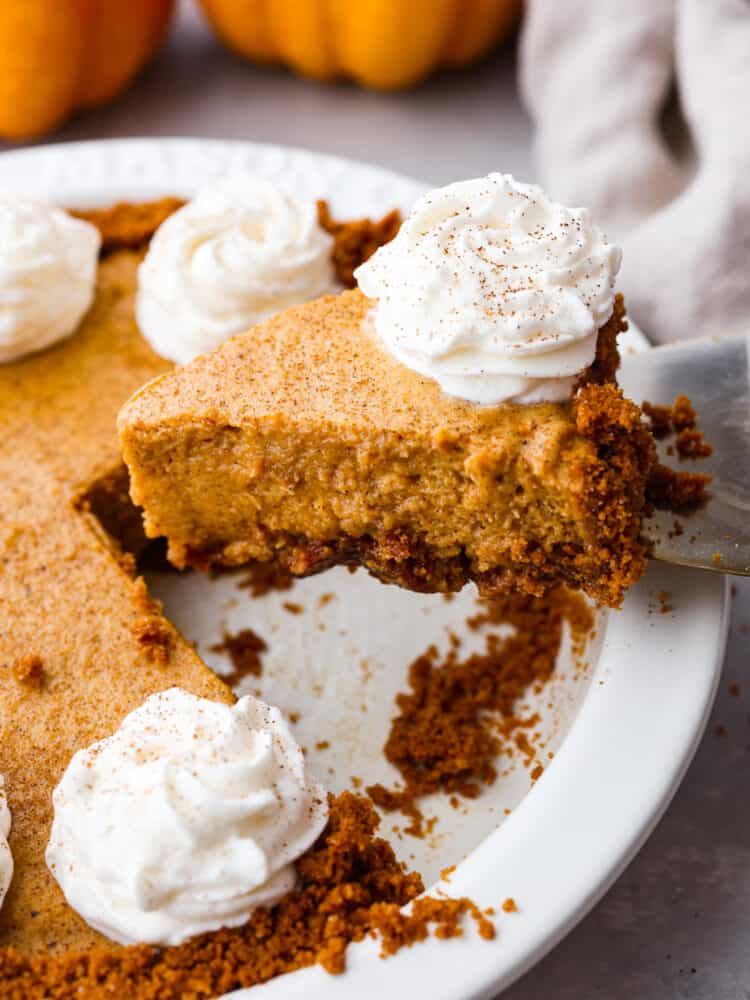A slice of Pumpkin Chiffon Pie with whipped cream sprinkled with cinnamon being scooped out of a white pie dish