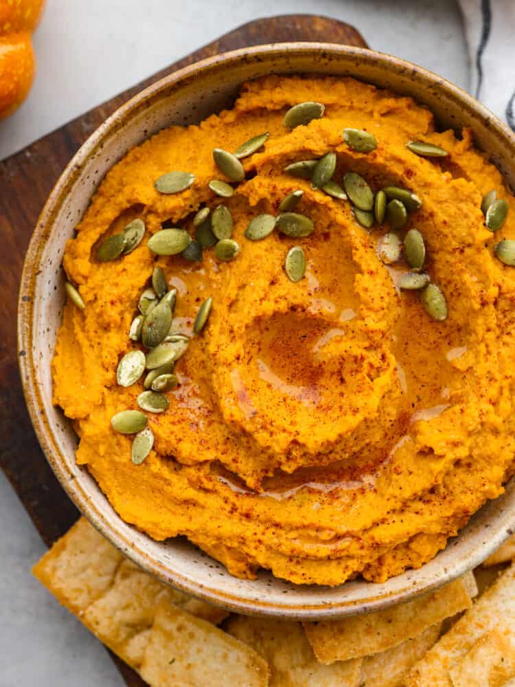 Top-down view of pumpkin hummus in a white bowl, garnished with pumpkin seeds.