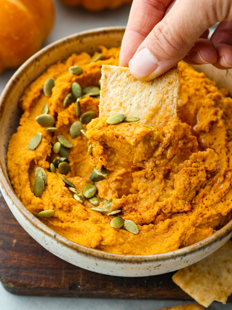 Closeup of a pita chip being dipped into a bowl of pumpkin hummus.