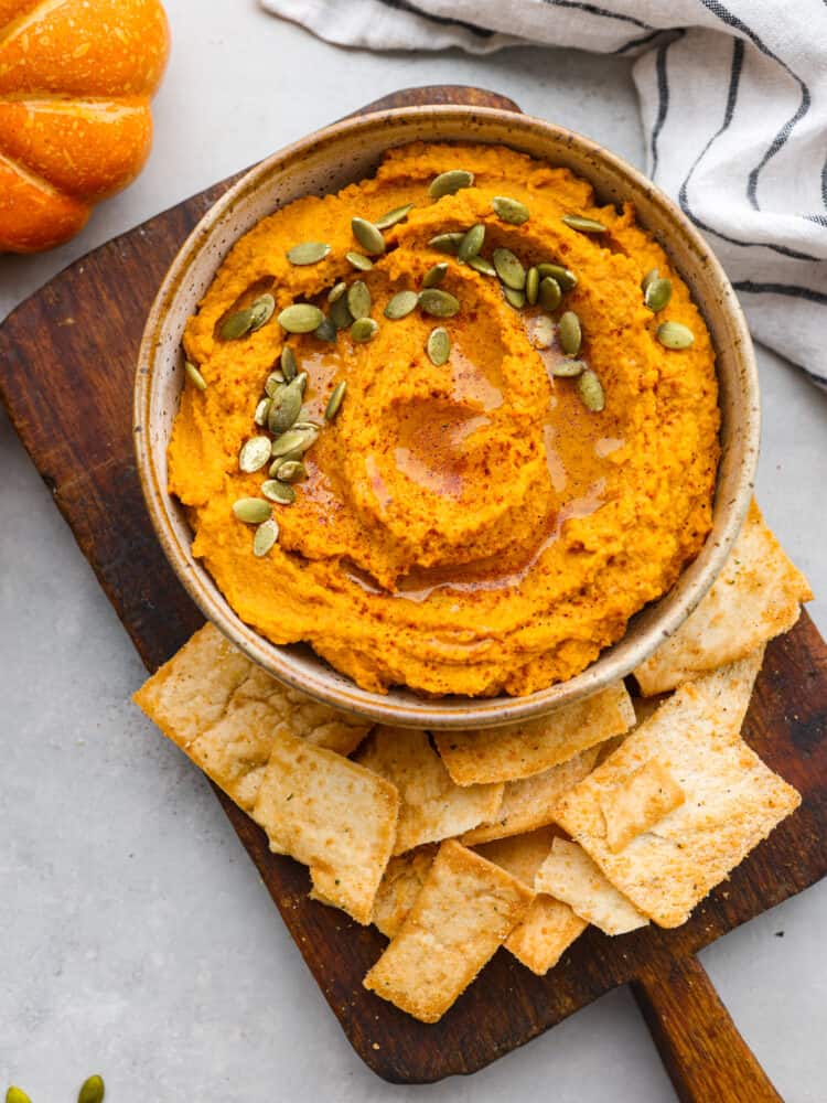 Pumpkin hummus served on a wooden tray with pita chips.
