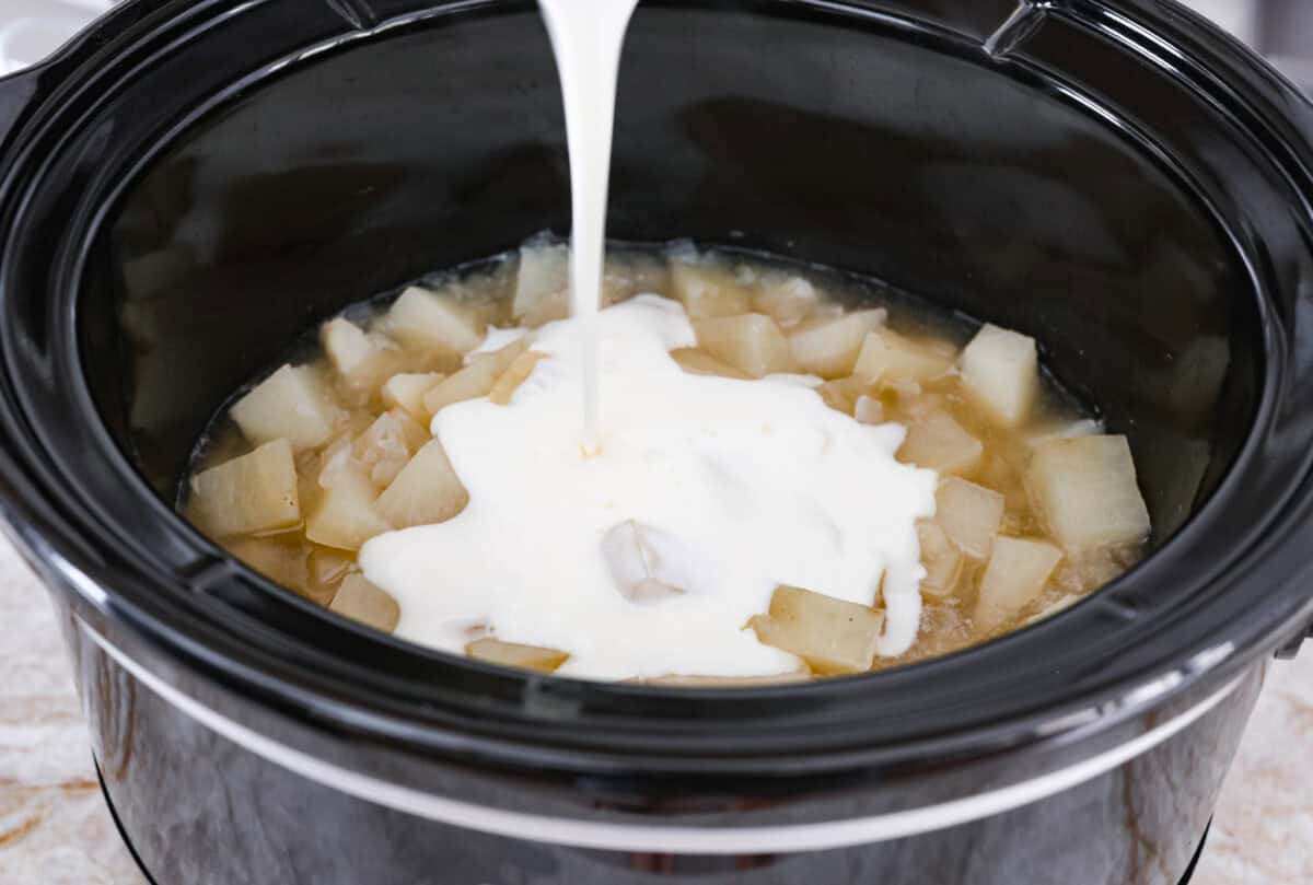 Overhead shot of cream and roux mixture being poured over the onion and potatoes in the slow cooker. 