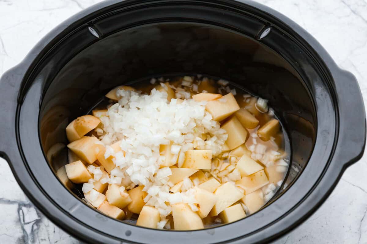 Overhead shot of potatoes, onions and chicken broth in slow cooker. 