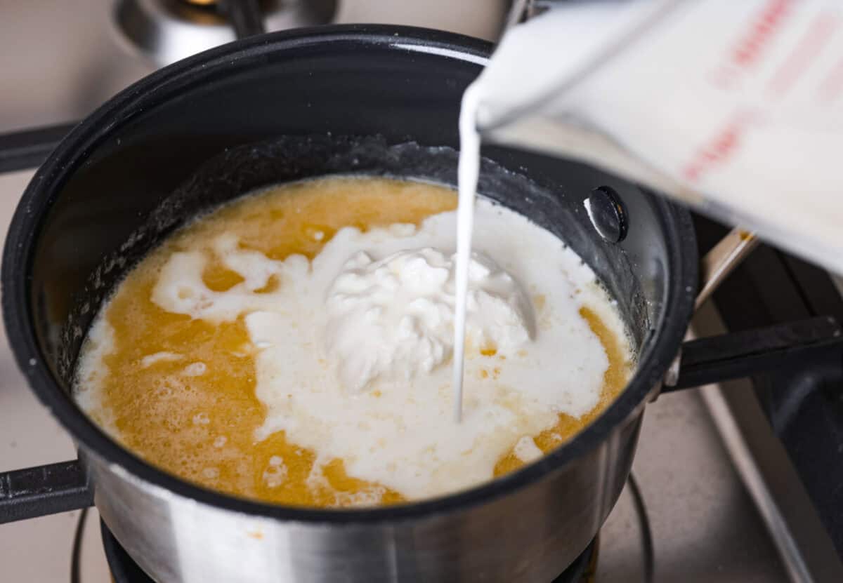 Overhead shot of sour cream and heavy whipping cream being poured into the roux.