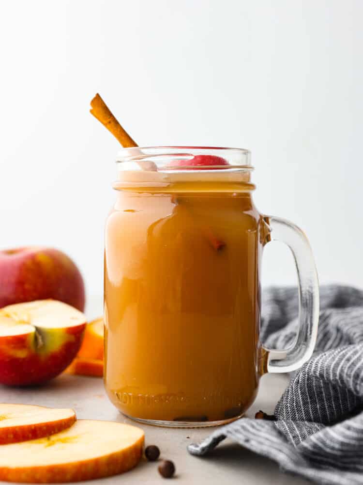 a mason jar with a handle filled with apple cider and topped with a cinnamon stick. 