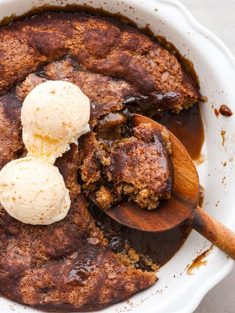 A close up of snickerdoodle cobbler being scooped out with a wooden spoon. A scoop of vanilla ice cream is on top. 