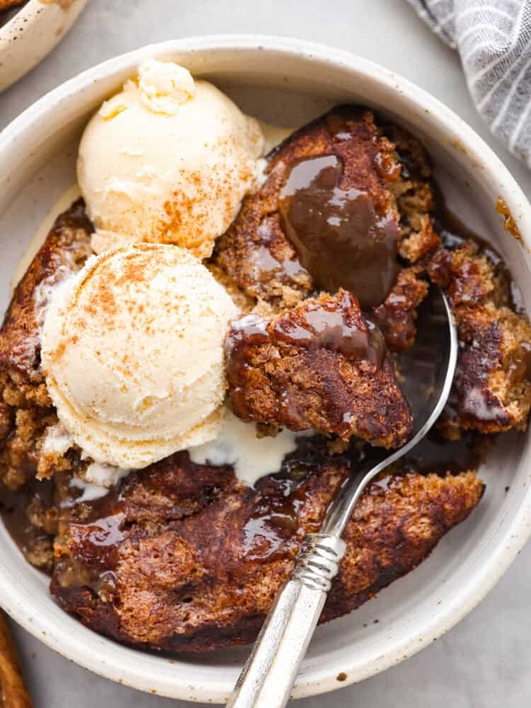 A closeup of snickerdoodle cobbler with ice cream and a silver spoon scooping some out of a white bowl. 