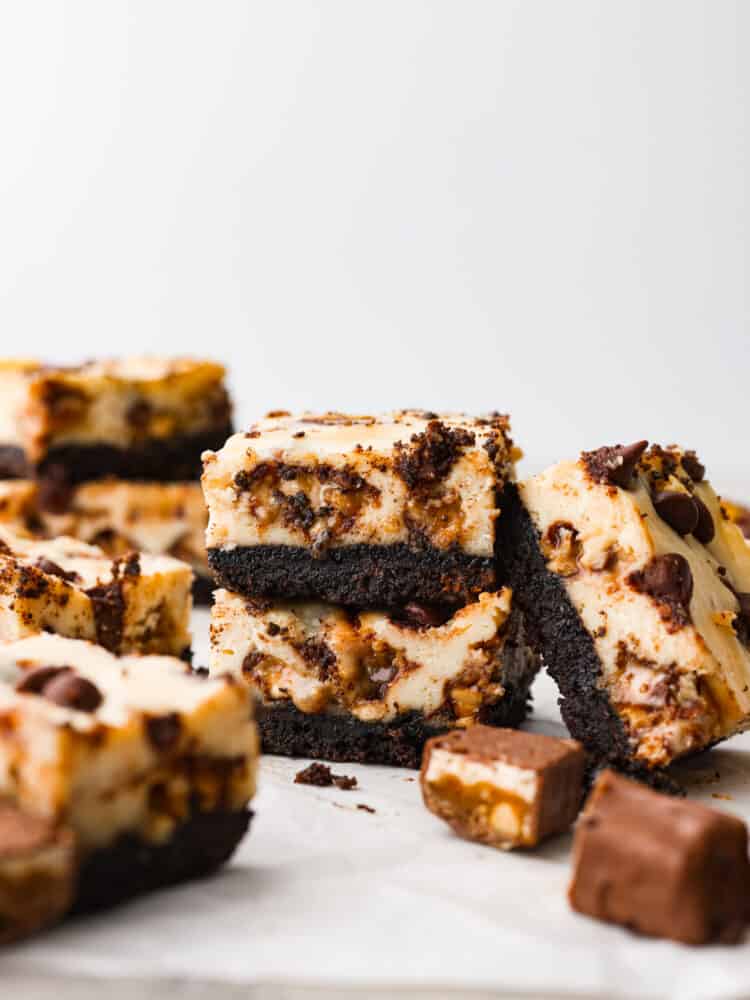 Snickers cheesecake bar slices stacked on top of each other. 