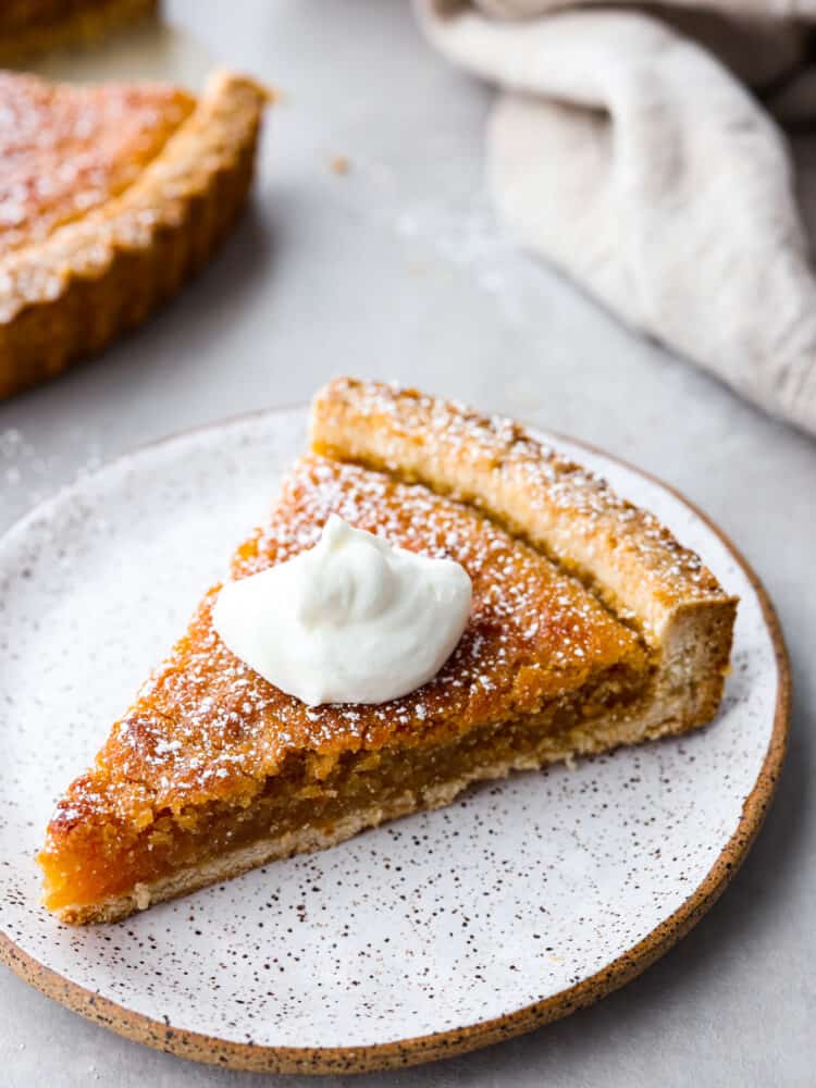 A slice of treacle tart with a dollop of whipped cream on top on a stone-like plate.