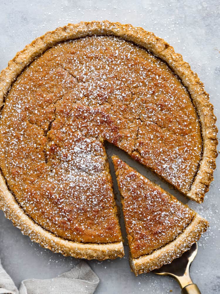 Treacle tart with powdered sugar sprinkled on top with a slice being lifted out.
