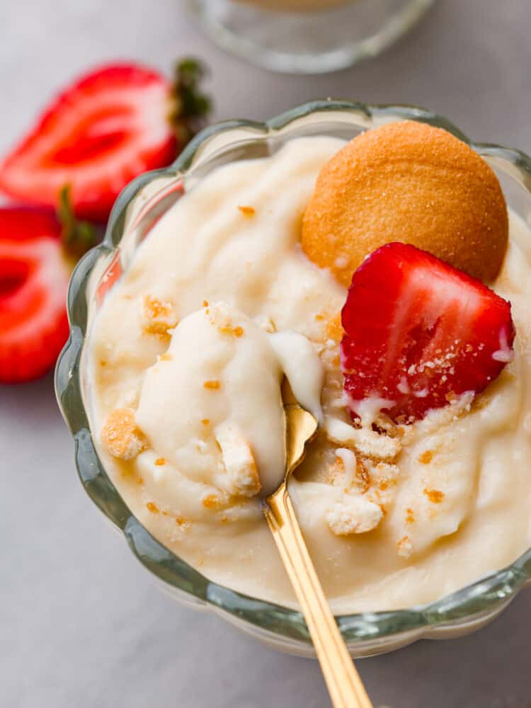Closeup of vanilla pudding in a glass cup topped with a Nilla Wafer and sliced strawberry.