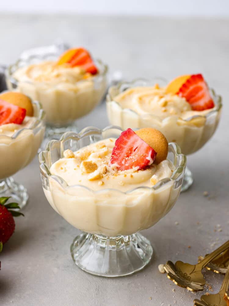 Vanilla pudding served in small glass cups garnished with sliced strawberries and cookies.