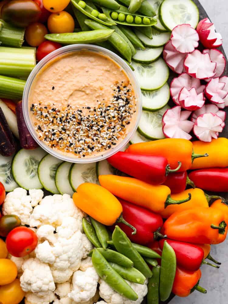 Top view of hummus surrounded by lots of veggies. Bagel seasoning is sprinkled on top of the hummus.