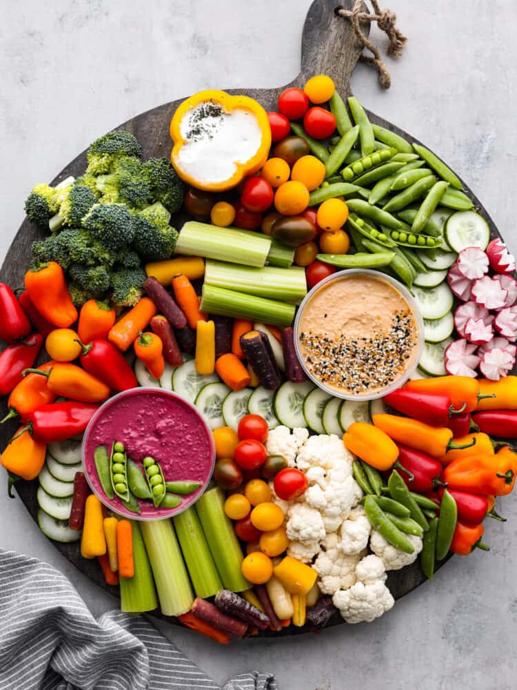 Top view of a veggie charcuterie workbench on a large round wood board. A kitchen towel is styled next to it.