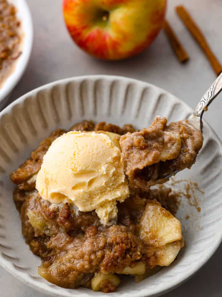 A slice of brown apple betty on a white ribbed plate with a fork taking a bite out of it.