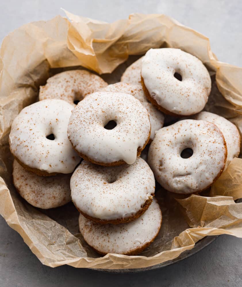 Glazed apple cider donuts in a bowl lined with parchment paper.