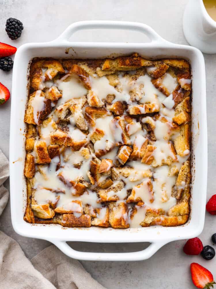 Bread pudding in a white pan with vanilla sauce on top.