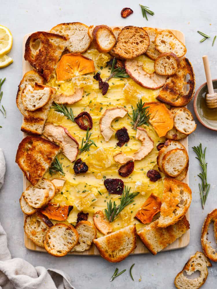 The overhead view of a butter board topped with dried fruits, rosemary sprigs and crostini. 