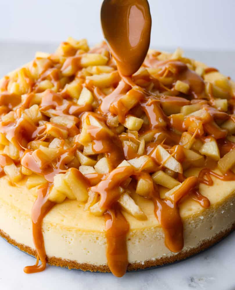 Caramel apple cheesecake with a spoon with caramel on it drizzling caramel over the top.