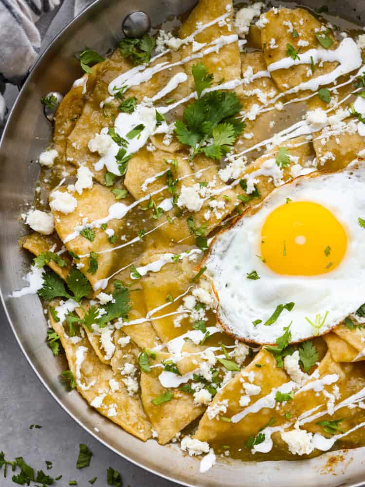 A close up of Chilaquiles in a pan that shows the cilantro, crema, and cheese on top.
