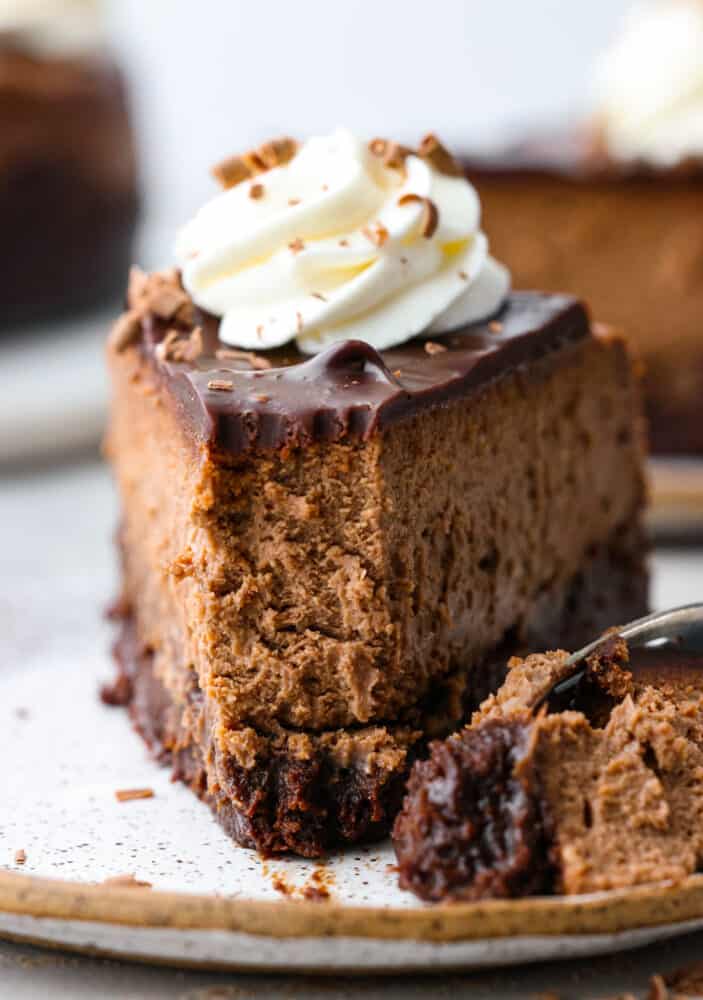 Front view of a slice of chocolate cheesecake with a bite taken out of it.