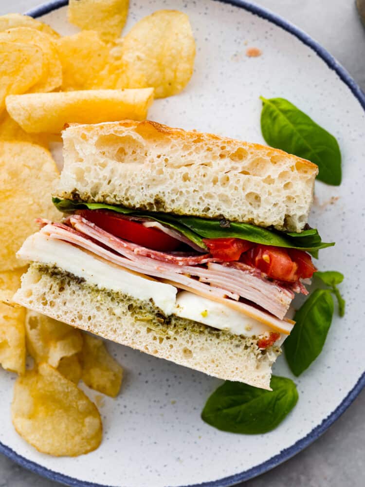 Sandwich on a plate with chips and basil next to it.