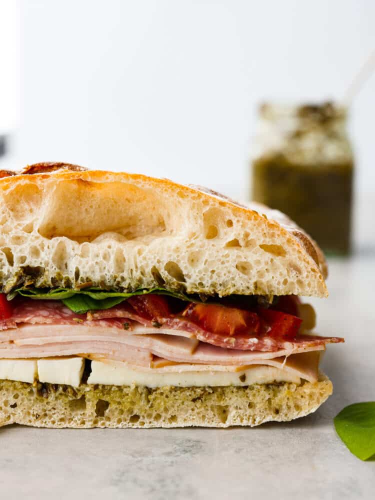 Ciabatta sandwich on a counter top with pesto in the background.