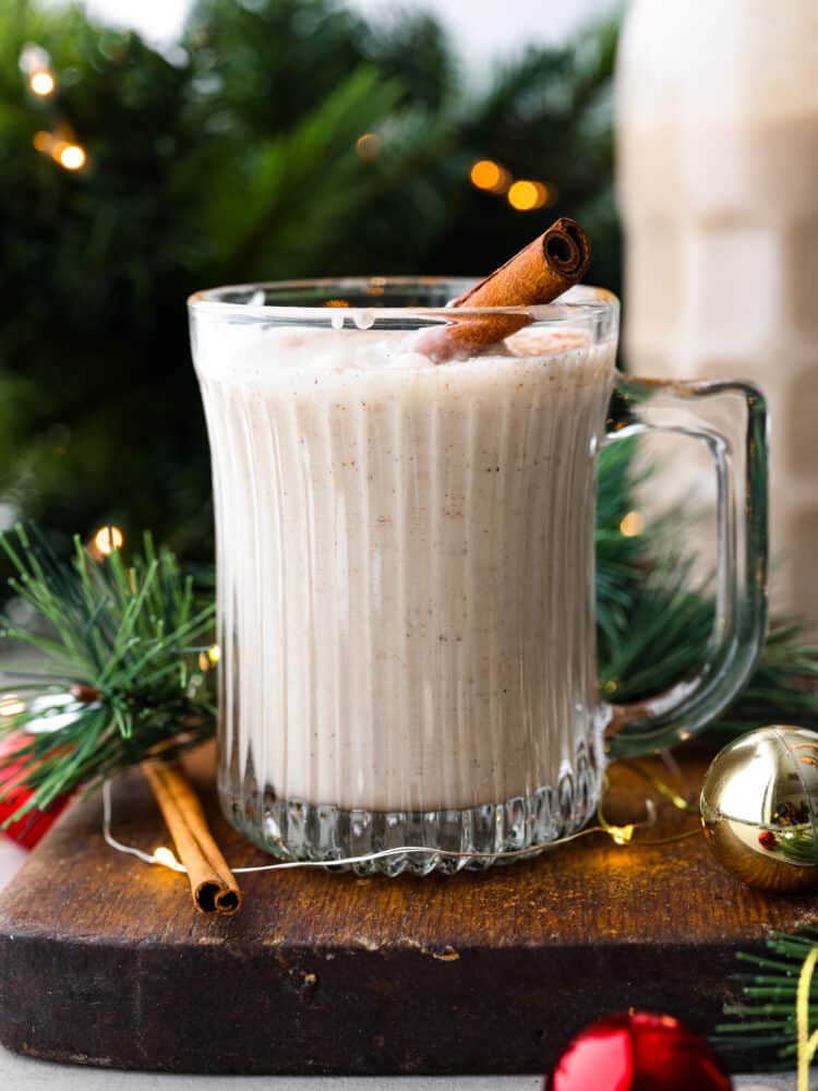 Coquito with a cinnamon stick in it and green branches behind it.