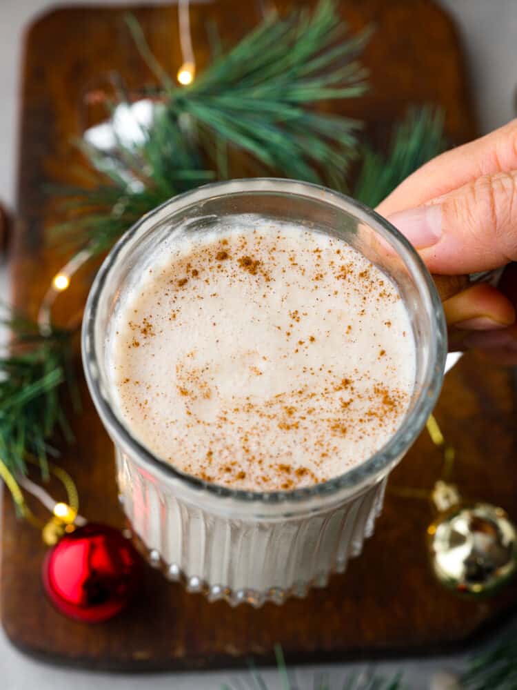 A hand holding coquito over a table.