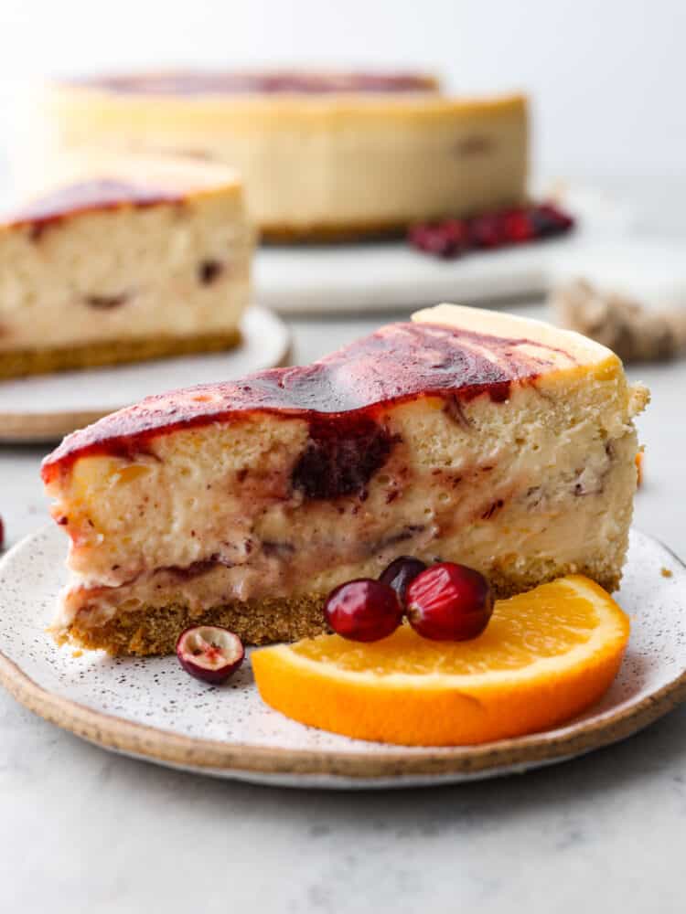 Cheesecake on a plate with cranberries and oranges in front of it.