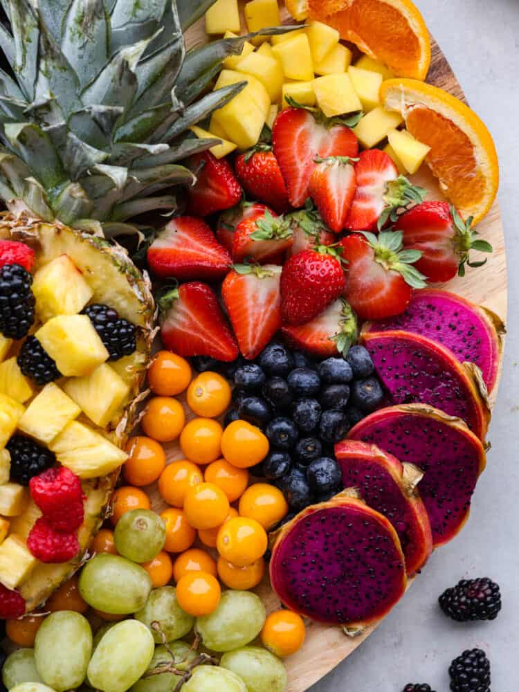 Close overhead view of the grapes, kumquat, dragonfruit, berries, pineapple, and orange slices on the charcuterie board. 