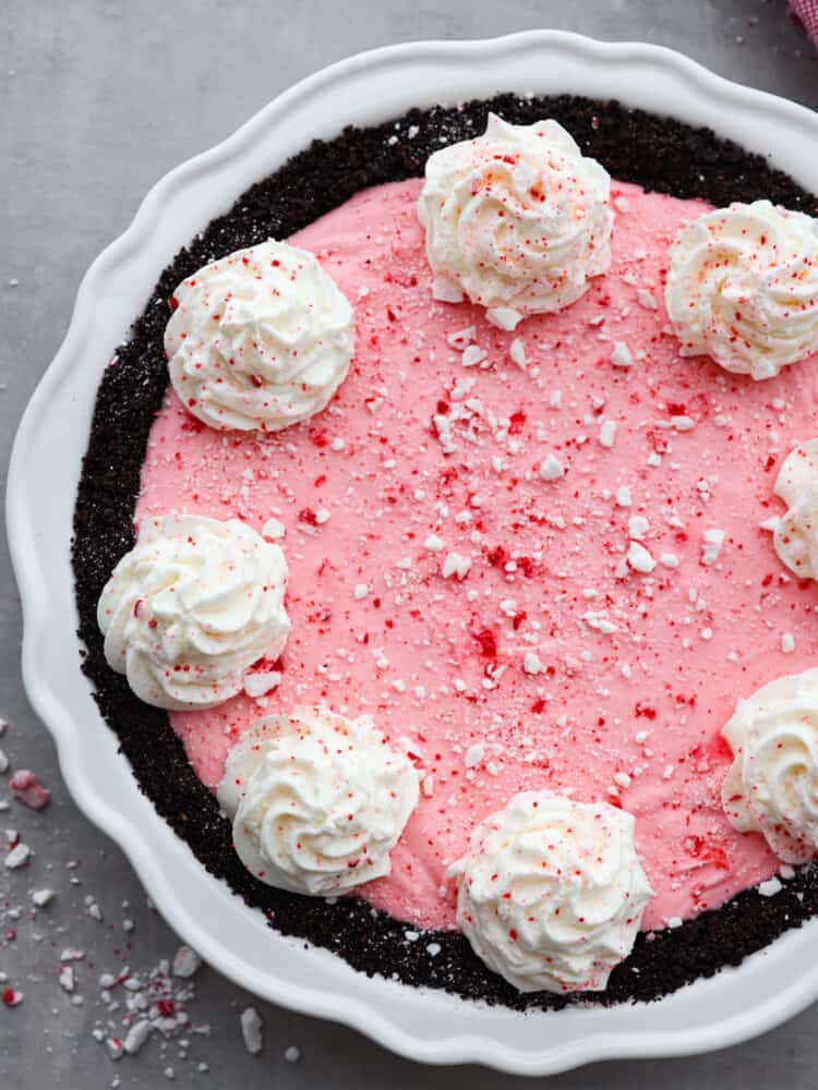 The top view of an order crust peppermint pie. garnished with dollops of whipped cream and crushed peppermint. 