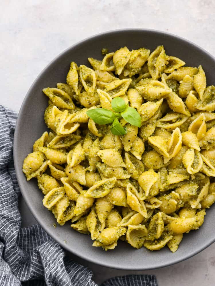 Top-down view of pesto pasta served in a gray bowl, garnished with herbs.