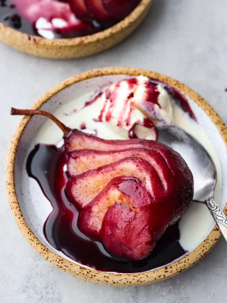 Poached pears on a plate with a spoon and ice cream next to it.